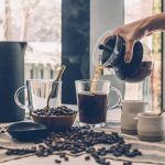 pouring brewed coffee in cup surrounded with coffee beans