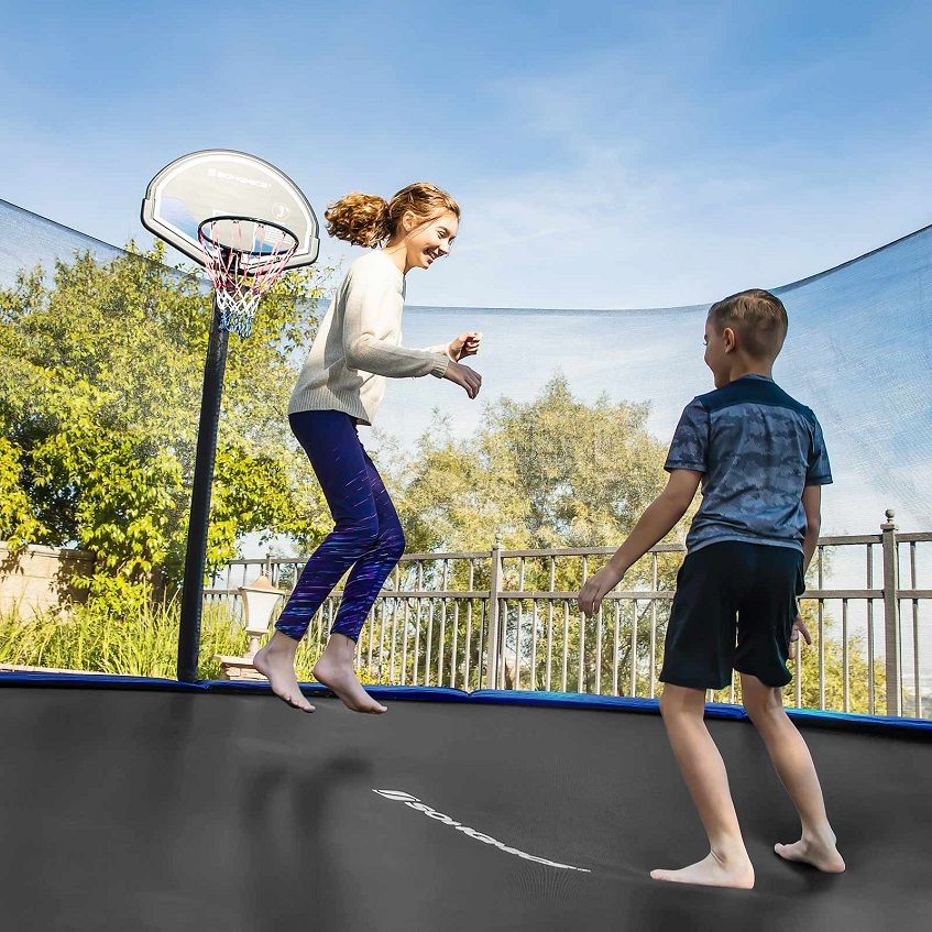 two kids jumping on a trampoline with a basketball hoop in it