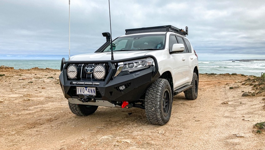 White Toyota Prado with bull bar and roof rack parked on the coast